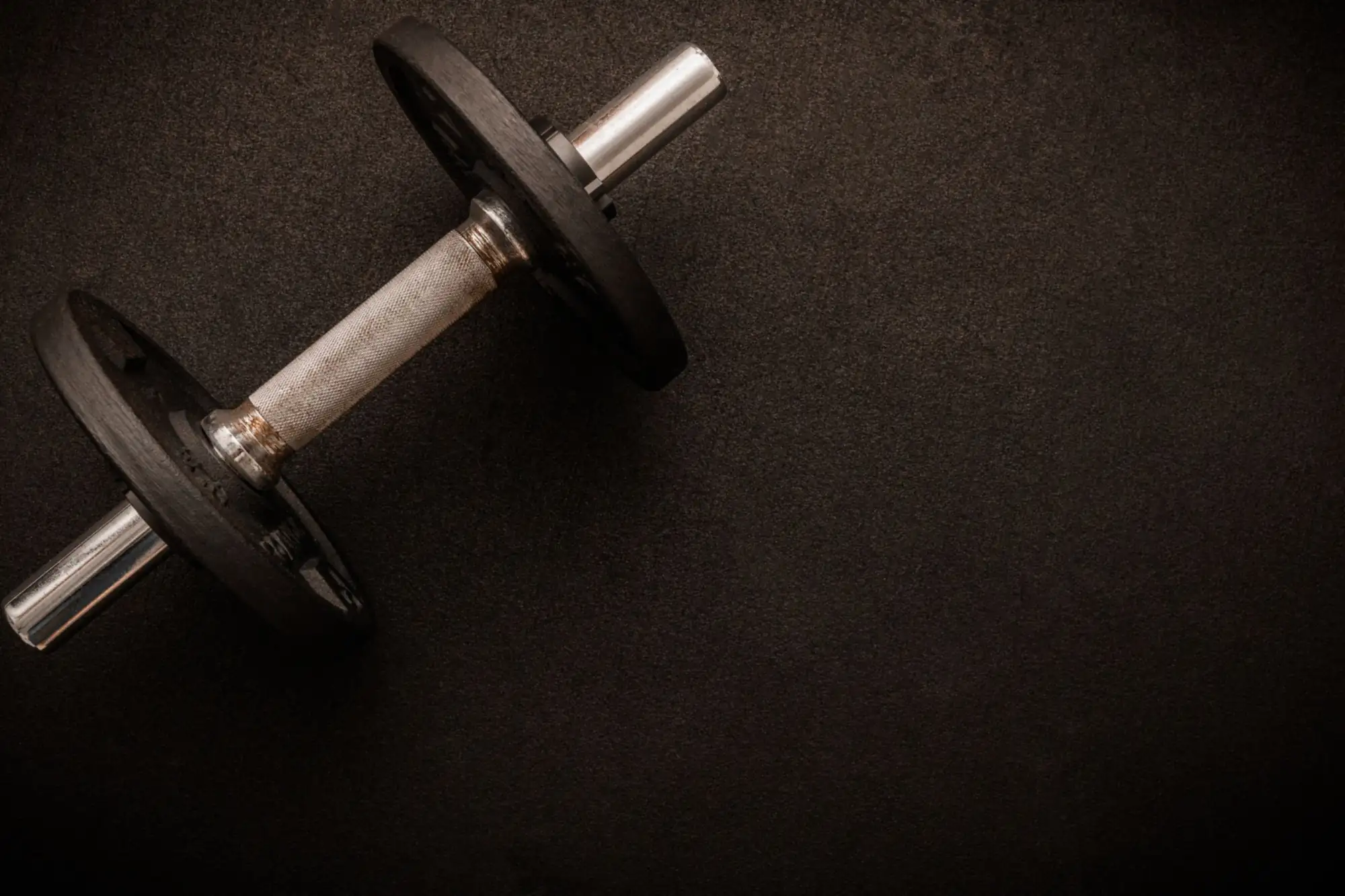 Una mancuerna sobre el suelo oscuro del gimnasio